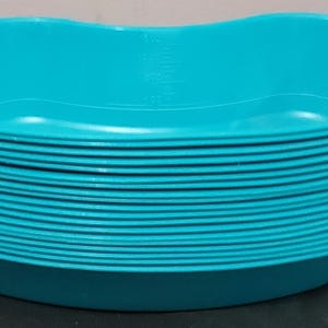 Puede incluir: Una pila de cuencos de plástico turquesa en forma de riñón. Los cuencos tienen un interior liso y un exterior estriado. La pila está sobre una superficie oscura. Los cuencos parecen nuevos y sin usar.