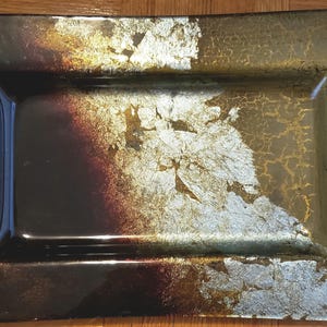 May include: Rectangular decorative tray with a glossy finish. The tray features a dark brown base with gold leaf accents and a rectangular recessed area. The edges are slightly raised, creating a defined border.