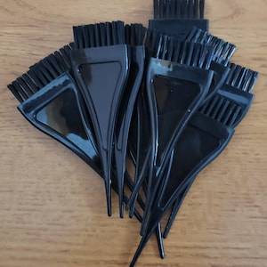 May include: A collection of black hair dye brushes with angled handles and bristled tips. The brushes are arranged in a fan-like pattern, showcasing their design and intended use for hair coloring or treatments.