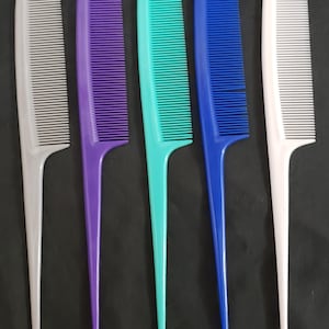 Puede incluir: Un conjunto de cinco peines de cola de plástico dispuestos en fila, que incluye un peine gris claro, morado, turquesa, azul y blanco. Cada peine tiene un mango largo y puntiagudo y una sección de dientes finos y juntos para peinar el cabello.