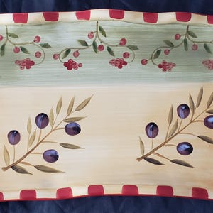 May include: Rectangular ceramic serving tray with a painted olive branch design. The tray has a cream-colored base with olive branches and purple olives. The top section is light green with red berries. The rim is red and white checkered.