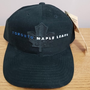 May include: A black baseball cap featuring the text "TORONTO MAPLE LEAFS" in blue and white. The cap has a structured crown and a curved brim. A maple leaf logo is embroidered on the front.