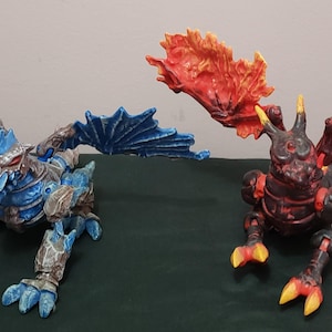 May include: Two fantasy dragon figurines. One is blue and silver, the other is red and black. Both have large, detailed wings and are posed in a crouching position. The dragons are detailed and appear to be made of a hard material.