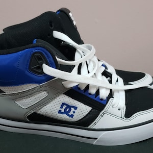 Può includere: Sneakers alte nere e bianche con dettagli blu e un logo DC bianco sul lato.