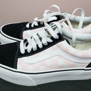 Peut inclure: Basket montantes Vans à plateforme en toile à carreaux noirs et roses avec lacets blancs. Les chaussures ont une épaisse semelle plateforme blanche.