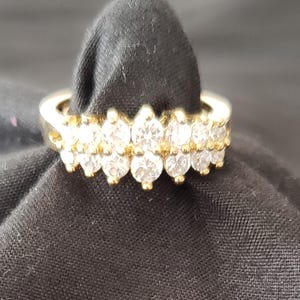 Peut inclure: Une bague en or présentant deux rangées horizontales de pierres claires taille ronde serties sur griffes. L'anneau est en or poli et les pierres sont disposées selon un motif symétrique sur le devant de la bague, créant un design multi-pierres.
