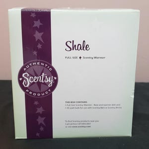 Puede incluir: Una caja de producto cuadrada blanca para un calentador Scentsy de tamaño completo Shale. La caja presenta una franja vertical morada en el lado izquierdo decorada con estrellas y el logotipo de Scentsy. El texto incluye detalles.