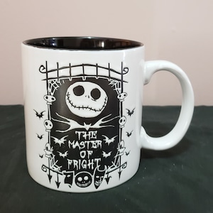 May include: White ceramic mug with a black interior and a wraparound design featuring Jack Skellington from The Nightmare Before Christmas. The design includes bats, skulls, and the text "THE MASTER OF FRIGHT."
