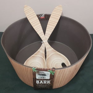 Könnte beinhalten: Eine braune und beige Salatschüssel mit passenden Salatbesteck. Die Schüssel hat eine dunkelbraune Innenseite und eine Holzmaserung außen. Das Salatbesteck ist hellbraun mit einem geschlitzten Design. Das Produktetikett lautet "BARK Bamboo Product".