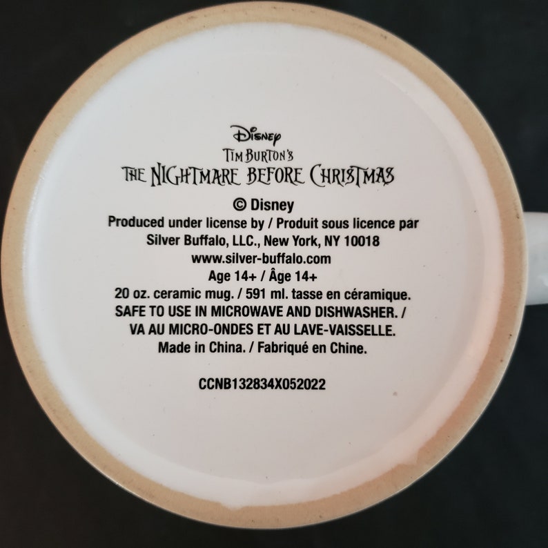 May include: A white ceramic mug with text from Tim Burton's The Nightmare Before Christmas. The text includes the Disney logo, production information, and care instructions. The mug is 20 oz.