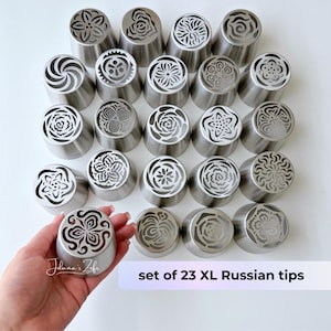 May include: A set of 23 XL Russian piping tips. The stainless steel tips feature various floral and decorative designs. One tip is held in a hand, showcasing the intricate patterns. The text "set of 23 XL Russian tips" is visible.