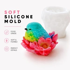 Puede incluir: Un molde de silicona blanco para fundición, acompañado de una figura terminada de un pequeño pájaro con plumas azules y amarillas descansando dentro de un grupo de flores de color rosa vibrante. El texto en la imagen dice SOFT SILICONE MOLD, FOOD GRADE, SOFT & FLEXIBLE y PERFECT DETAILS.