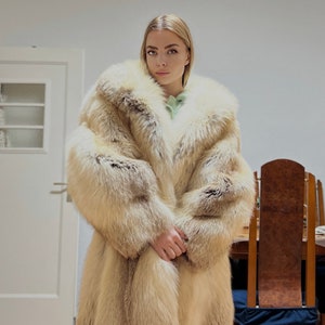 May include: A long fur coat in cream and tan hues. The coat has a large, fluffy collar and full sleeves. The fur looks soft and thick, creating a warm and elegant shape. This coat is a statement piece, ideal for the colder months.