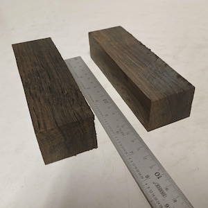May include: Two rectangular blocks of dark brown wood with visible grain patterns, positioned next to a metal ruler. The ruler shows the blocks are approximately 12.7 cm long and 3.8 cm wide, with a thickness of about 3.8 cm.