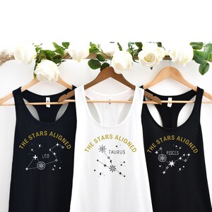 May include: Three tank tops with the text "The Stars Aligned" and a constellation design. The tank tops are black, white, and black. The constellations are Leo, Taurus, and Pisces.