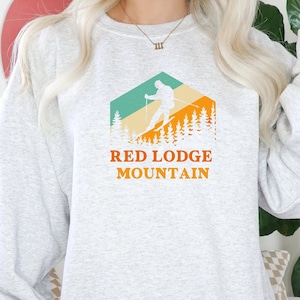May include: A gray sweatshirt with a retro-style graphic of a skier in a mountain landscape. The graphic includes the text "Red Lodge Mountain".
