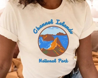 Op de afbeelding: Een wit T-shirt met een blauwe en bruine afbeelding van het Channel Islands National Park. De afbeelding toont een bergketen en de oceaan.