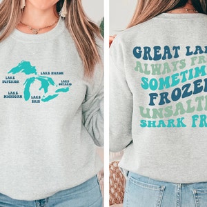 May include: Gray sweatshirt with a blue outline of the Great Lakes and the names of each lake on the front. The back of the sweatshirt has the text "Great Lakes Always Fresh Sometimes Frozen Unsalted Shark Free" in a rainbow of colors.
