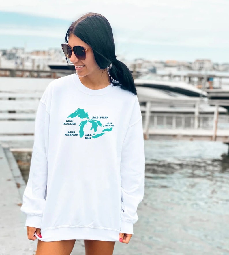 May include: White sweatshirt with a teal outline of the Great Lakes and the names of each lake: Lake Superior, Lake Huron, Lake Michigan, Lake Erie, and Lake Ontario.
