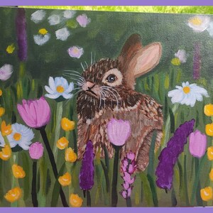 May include: An acrylic painting on canvas featuring a brown rabbit centered in a lush green meadow filled with colorful wildflowers. The scene includes purple lavender stalks, bright yellow blossoms, white daisies, and soft pink tulip-like flowers.