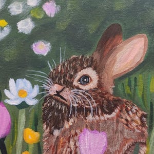 May include: An oil painting of a brown rabbit with long ears and white whiskers, positioned in a lush green meadow filled with colorful flowers including white daisies, yellow centers, and vibrant pink and purple blossoms in the foreground.