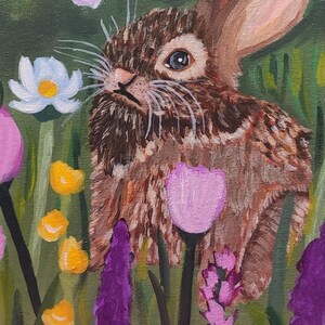 May include: An acrylic painting of a brown rabbit with textured fur standing in a field of colorful wildflowers. The scene features white daisies with yellow centers, pink tulips, purple spikes, and small yellow blossoms against a green background.