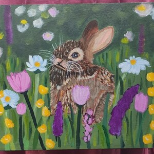 May include: An acrylic painting on canvas depicting a brown rabbit sitting in a field of colorful wildflowers. The scene features purple, pink, white, and yellow flowers set against a dark green background with visible brushstrokes throughout.