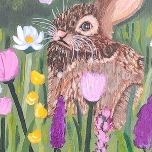 May include: An acrylic painting of a brown rabbit with textured fur sitting in a vibrant meadow. The scene features white daisies, pink tulips, small yellow wildflowers, and tall purple stalks set against a lush green background.