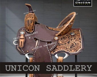 May include: A brown leather saddle with intricate floral tooling and a tooled leather skirt. The saddle is on a metal stand and has a silver stirrup.