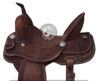May include: A brown leather saddle with intricate tooling and silver accents. The saddle features a  "Unicon Saddlery Horse Paradise" logo.