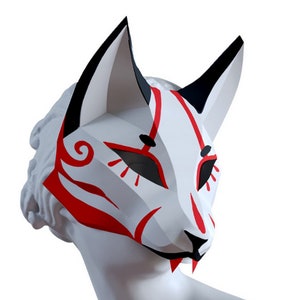 Peut inclure: Un masque de renard blanc avec des accents rouges et noirs. Le masque pr&eacute;sente un visage de renard stylis&eacute; avec un motif en spirale sur le front et un nez pointu.