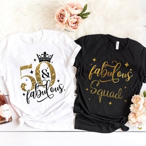 Pode incluir: Duas camisetas com texto em glitter dourado. Uma camiseta branca diz "50 & fabulous" com uma coroa acima do 50. A outra camiseta preta diz "fabulous squad".