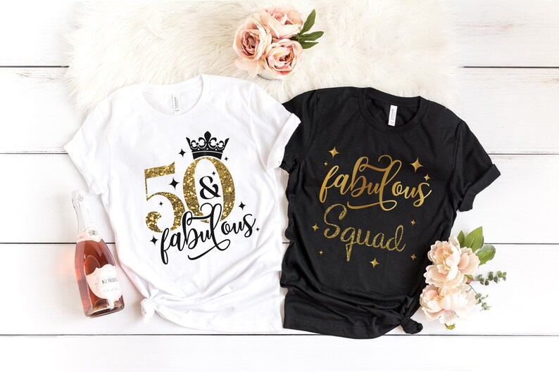 Pode incluir: Duas camisetas com texto em glitter dourado. Uma camiseta branca diz "50 & fabulous" com uma coroa acima do 50. A outra camiseta preta diz "fabulous squad".