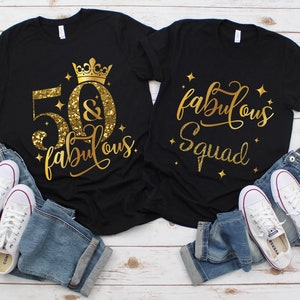Pode incluir: Duas camisetas pretas com texto em glitter dourado. Uma camiseta diz "50 & fabulous" com uma coroa dourada acima do 50. A outra camiseta diz "fabulous squad".