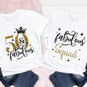 Pode incluir: Duas camisetas brancas com texto em glitter dourado. Uma camiseta diz "50 & fabulous" com uma coroa acima do 50. A outra camiseta diz "fabulous squad".