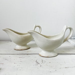 Op de afbeelding: Twee witte keramische sausbooten met een klassiek ontwerp. De boten hebben een ronde basis en een tuit om te gieten.