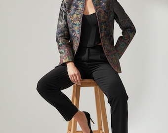 May include: A structured blazer featuring a dark, multi-colored paisley pattern with black leather-look sleeves, worn over a black corset-style top and black tailored trousers, paired with black pointed-toe high heels and dark spherical earrings.