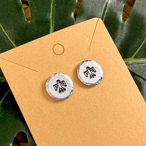 May include: A pair of silver stud earrings with a black stylized bird design. The earrings are displayed on a brown card.
