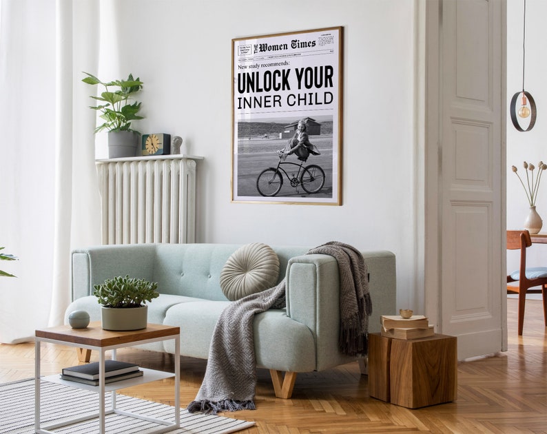 May include: A black and white photo of a woman riding a bicycle. The photo is framed and hanging on a white wall. The photo is titled "Unlock Your Inner Child" and is from the "Women Times" newspaper.