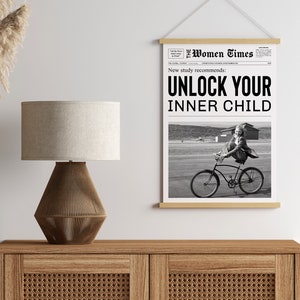 May include: Black and white newspaper print with the headline "Unlock Your Inner Child" and a photo of a girl riding a bicycle. The newspaper is framed and hanging on a wall.