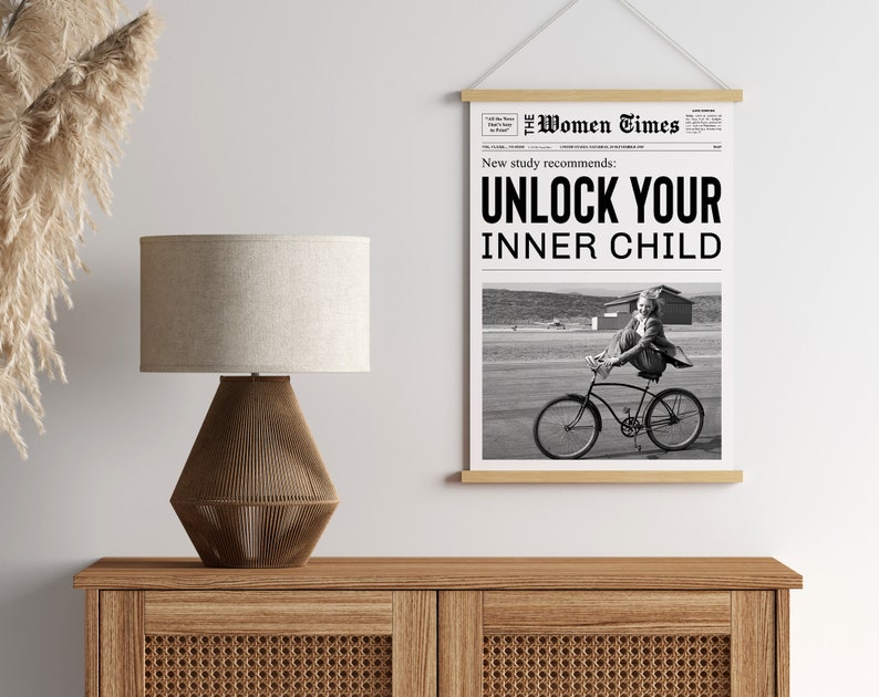 May include: Black and white newspaper print with the headline "Unlock Your Inner Child" and a photo of a girl riding a bicycle. The newspaper is framed and hanging on a wall.