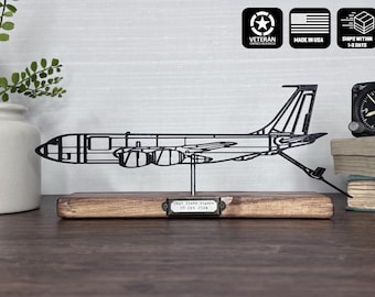 May include: Black metal airplane sculpture mounted on a wooden base. The sculpture has a detailed outline of an aircraft. The base includes a small metal plate with text. A vintage clock and books are in the background.