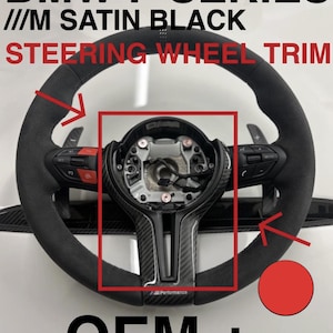 May include: Black steering wheel trim with the text "BMW F SERIES ///M SATIN BLACK STEERING WHEEL TRIM OEM +". The wheel features red accents and a carbon fibre centre.