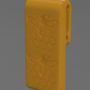 May include: A yellow rectangular object with a curved top and a clip on the side. The front features two embossed bee and honeycomb designs. The object is a solid, bright yellow color.
