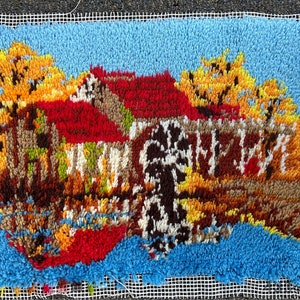 Könnte beinhalten: Ein bunter Teppich, der ein Haus mit rotem Dach und eine Windmühle zeigt, umgeben von Bäumen mit gelben Blättern. Der Teppich ist aus Garn gefertigt und hat eine strukturierte Oberfläche.