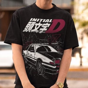 Peut inclure: T-shirt noir avec un imprimé graphique blanc et rouge d'une voiture et le texte "INITIAL D" en japonais et en anglais.