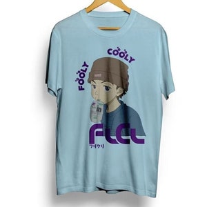 Puede incluir: Camiseta azul claro con una ilustración de estilo anime de una persona bebiendo de un cartón. La camiseta tiene las palabras "FOOLY COOLY" y "FCL" en morado, con texto japonés debajo. La persona lleva un gorro marrón.