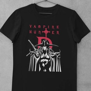 Puede incluir: Camiseta negra con un diseño gráfico en blanco y rojo de un cazador de vampiros. El diseño incluye una figura de cazador de vampiros con una espada, una cruz y las palabras "VAMPIRE HUNTER". La camiseta está colgada en una percha.