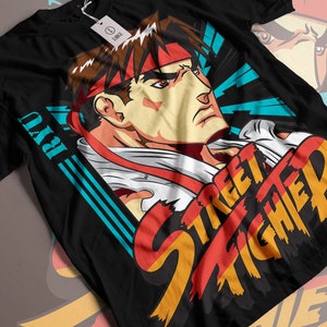 May include: Black t-shirt with a retro-style illustration of a character from the Street Fighter video game series. The character has brown hair and is wearing a red headband. The text "Street Fighter" is written in a stylized font in yellow, orange, and red.