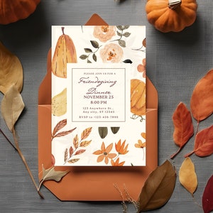 Puede incluir: Una tarjeta de invitación blanca con un diseño floral y de calabaza. El texto en la tarjeta dice "Por favor, únase a nosotros para una cena de Acción de Gracias entre amigos, el 25 de noviembre a las 8:00 PM, 123 Anywhere St..., Any city, ST 12345, RVSP al 123-456-7890". La tarjeta está en un sobre marrón con hojas de otoño esparcidas a su alrededor.